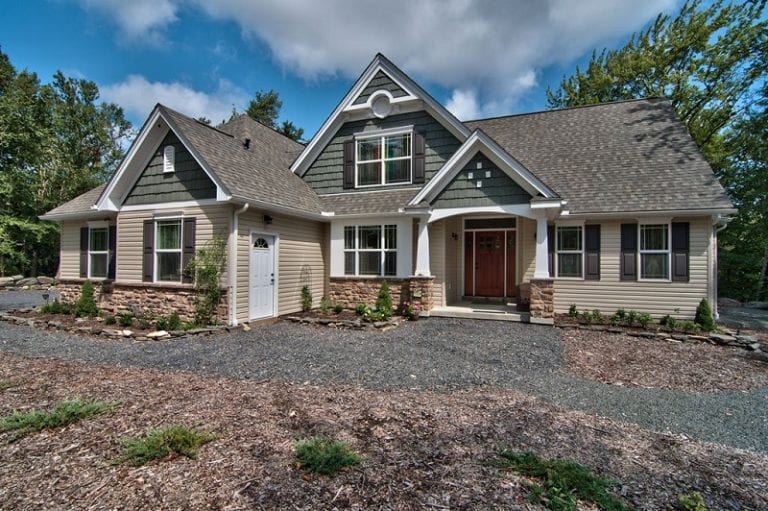 Custom home front exterior with tan siding, dark green shake and pillared entrance